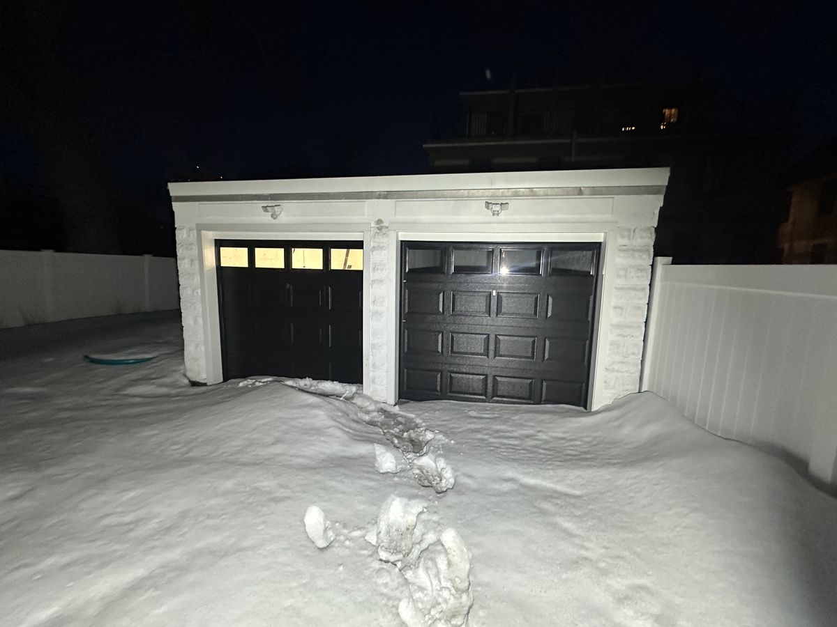 Two black garage doors with windows on white garage in snowy winter setting