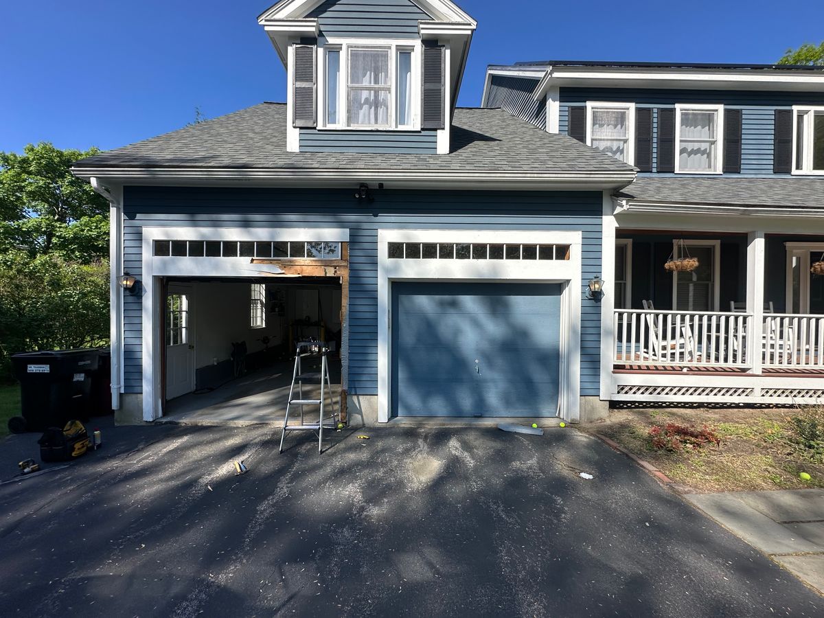 Blue garage door installation in progress on colonial home with ladder visible